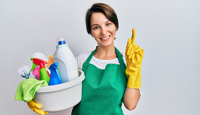 Home 5 Happy cleaner holding cleaning supplies, pointing up for satisfaction guarantee